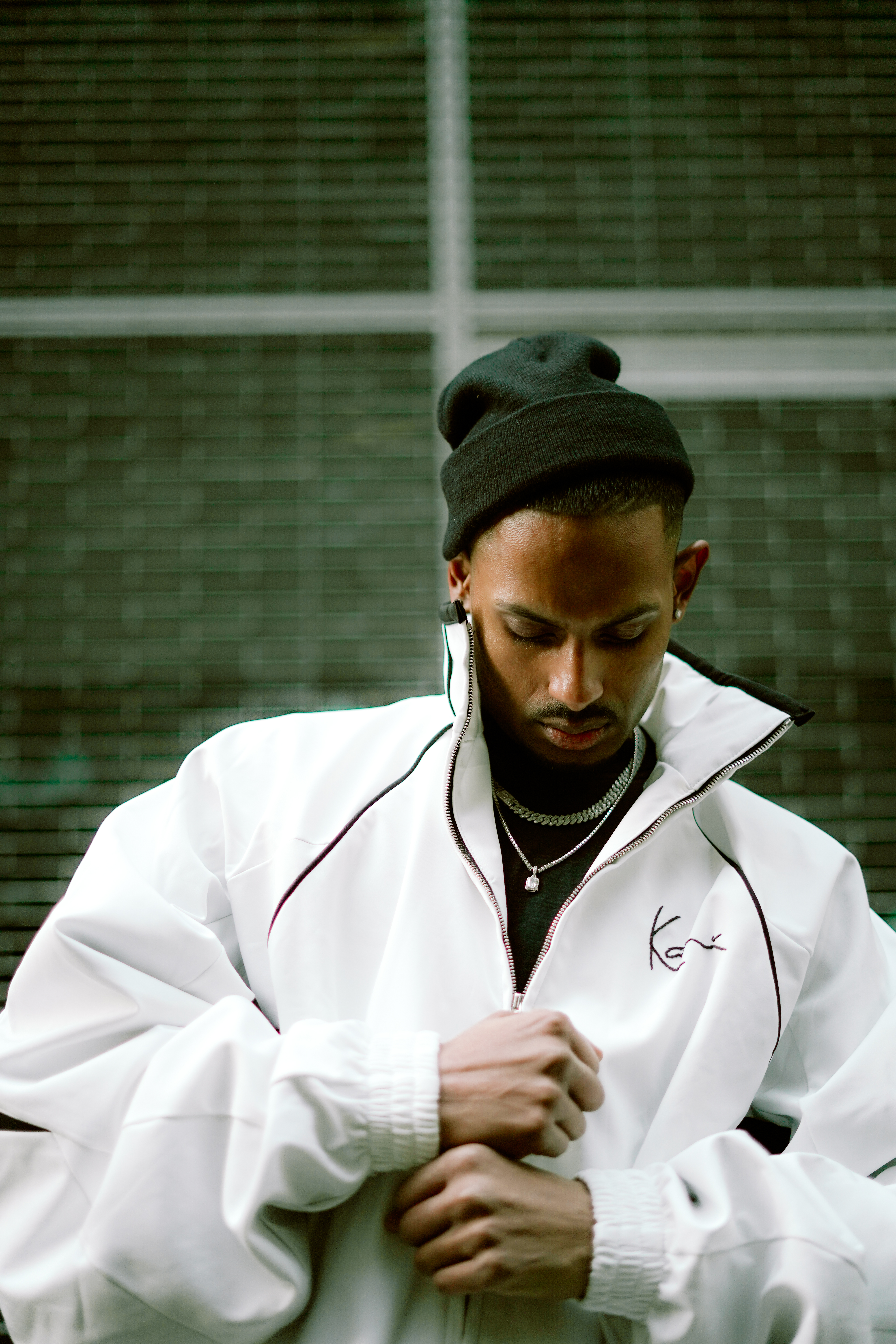 NIJO in white Karl Kani Shot Clock tracksuit jacket, beanie, court-style backdrop